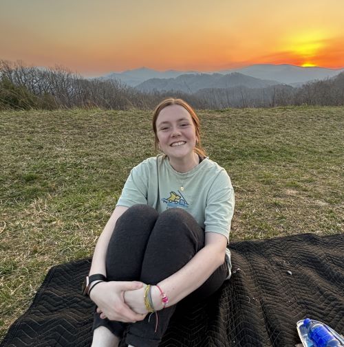 Student sitting in front of mountain sunset
