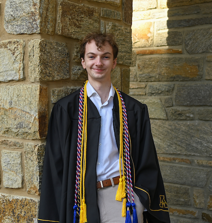 Hermes Henry wearing commencement regalia and leaning against a stone pillar.